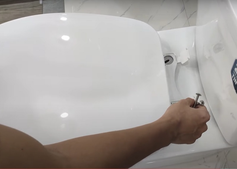 Căn chỉnh các lỗ của nắp bồn cầu, đặt vòng đệm inox vào lỗ rồi đặt vít vào lỗ